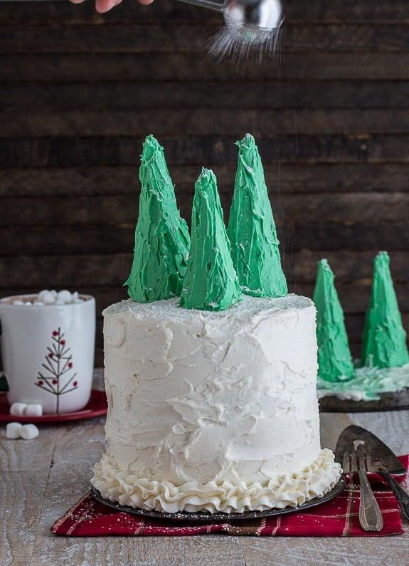 Fetta di torta di pan di zenzero umida e speziata, ricoperta di crema al burro alla vaniglia e coronata da festivi alberi di Natale commestibili