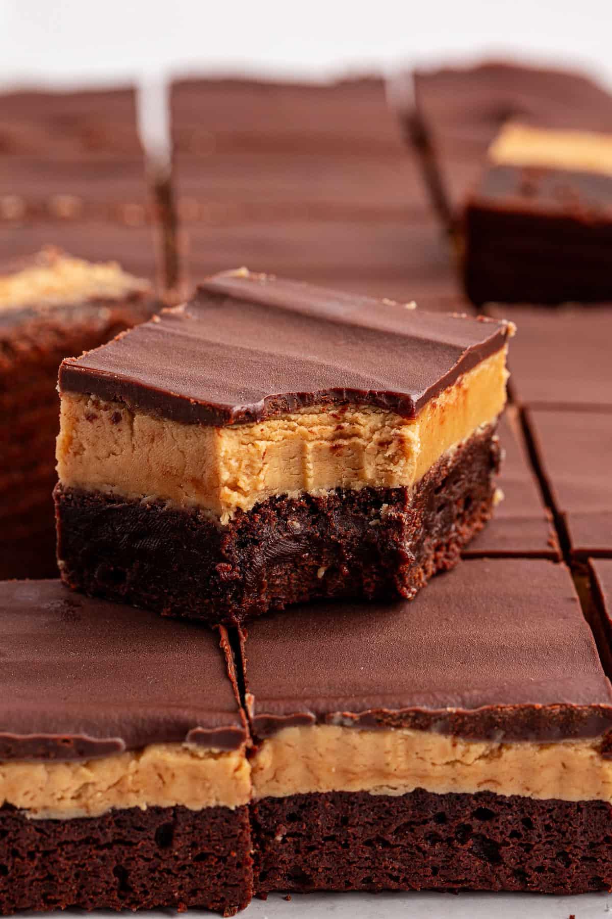 Primo piano di brownies Buckeye a strati di cioccolato e burro d'arachidi, con un brownie in cima che mostra un morso preso, rivelando gli strati cremosi di burro d'arachidi e il ricco cioccolato.