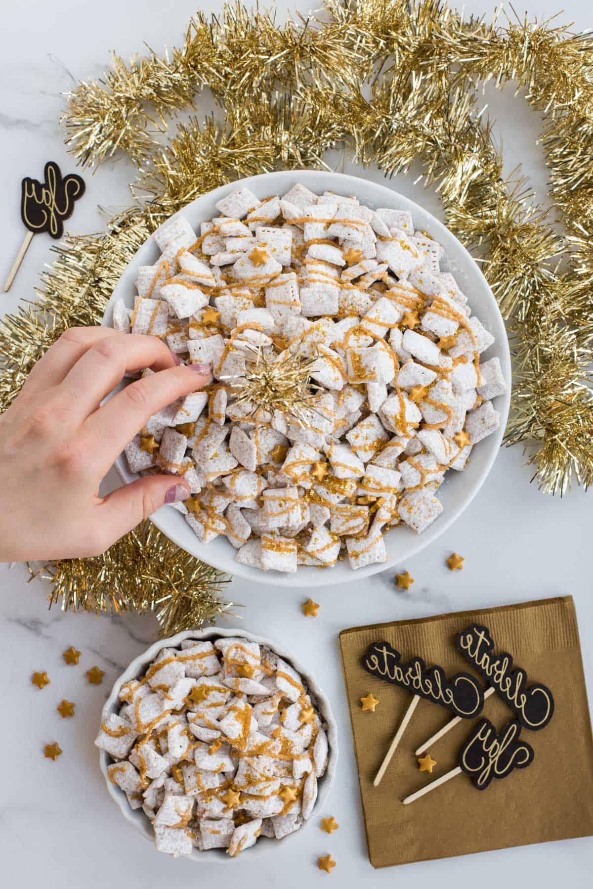 **Dolcetti Croccanti al Cioccolato Bianco di Capodanno** 3 new year’s eve white chocolate puppy chow with gold sprinkles and gold stars on a white background