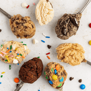 **Semplice Impasto per Biscotti Commestibile** 21 seven spoons in a circle with different flavors of edible cookie dough with m&ms, chocolate chips and sprinkles scattered around