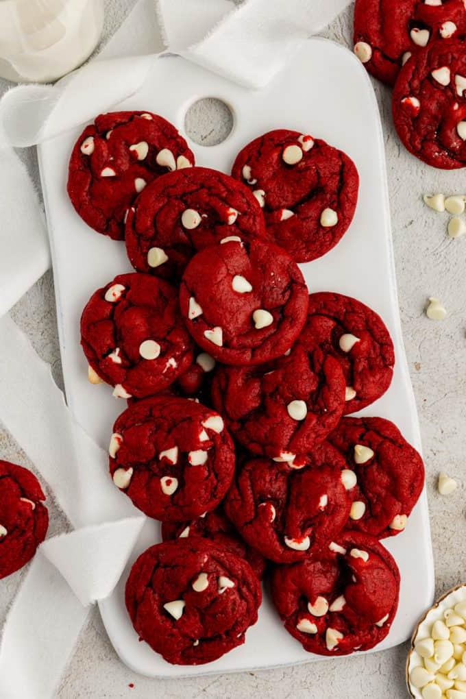 Fare Biscotti dal Mix per Torte 21 Biscotti Red Velvet con preparato per torte su un tagliere bianco circondato da gocce di cioccolato bianco sparse e altri biscotti