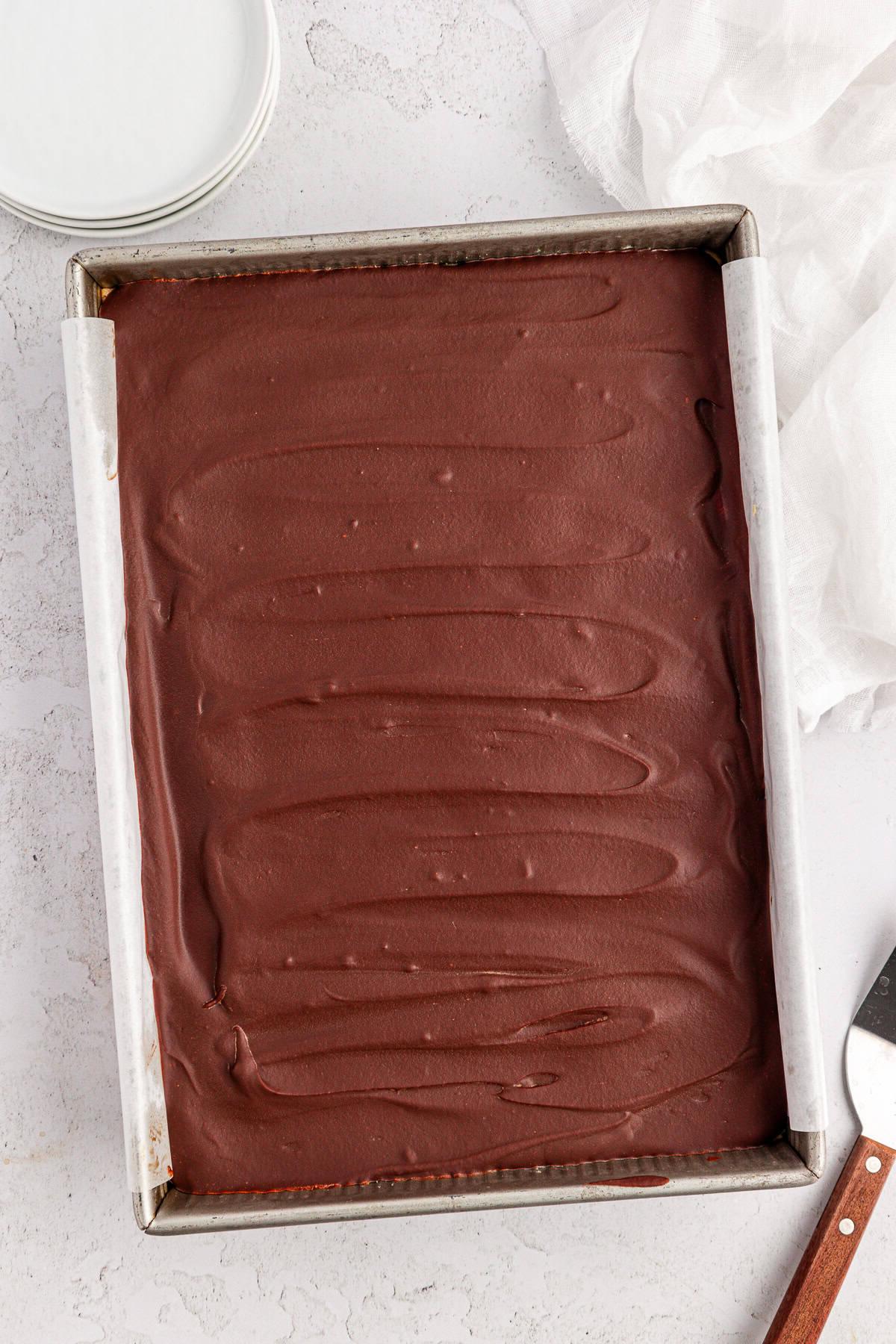 Una teglia da forno rettangolare piena di brownies Buckeye, posta su una superficie chiara con una stoffa bianca, piatti rotondi e un server per torte nelle vicinanze.