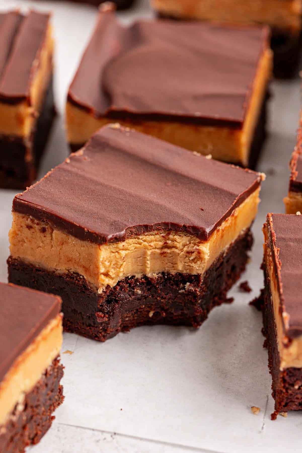 Un primo piano di brownies Buckeye a strati di cioccolato e burro d'arachidi, con un pezzo che mostra un morso preso, rivelando spessi strati di brownie fondente, burro d'arachidi cremoso e morbida copertura di cioccolato.