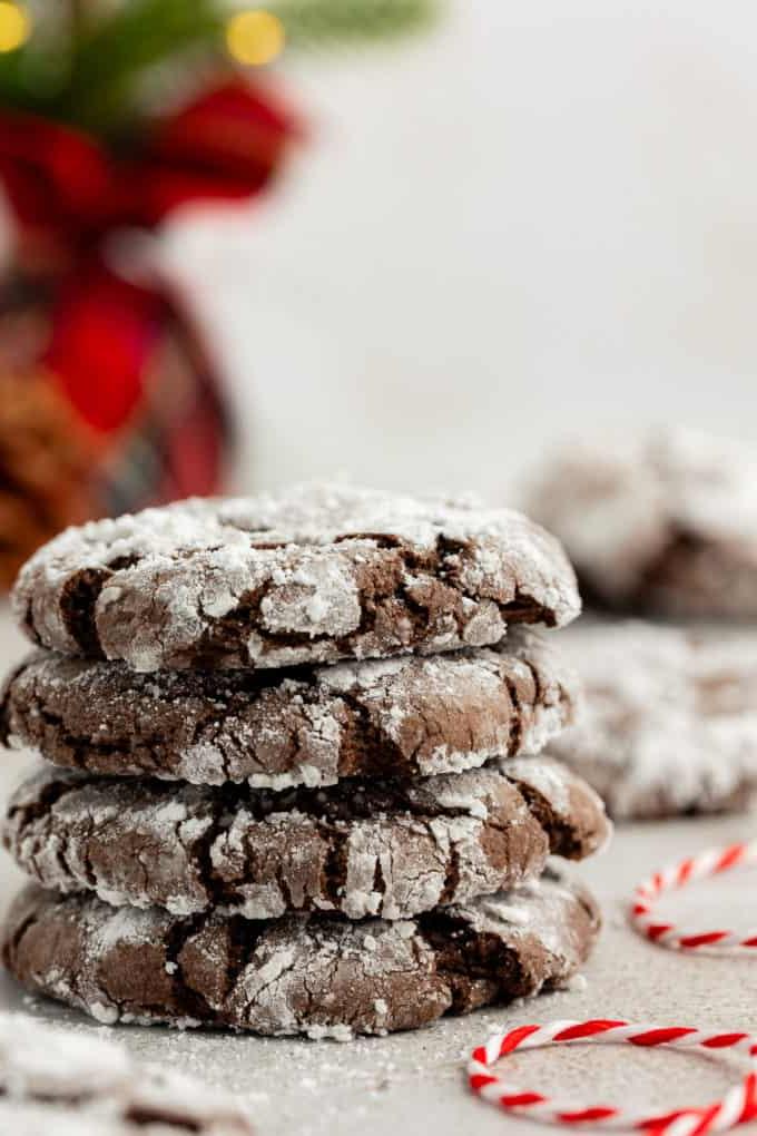 Fare Biscotti dal Mix per Torte 25 4 biscotti Chocolate Crinkle con preparato per torte impilati con zucchero a velo sparso intorno, uno spago bianco e rosso accanto alla pila e altri biscotti sullo sfondo
