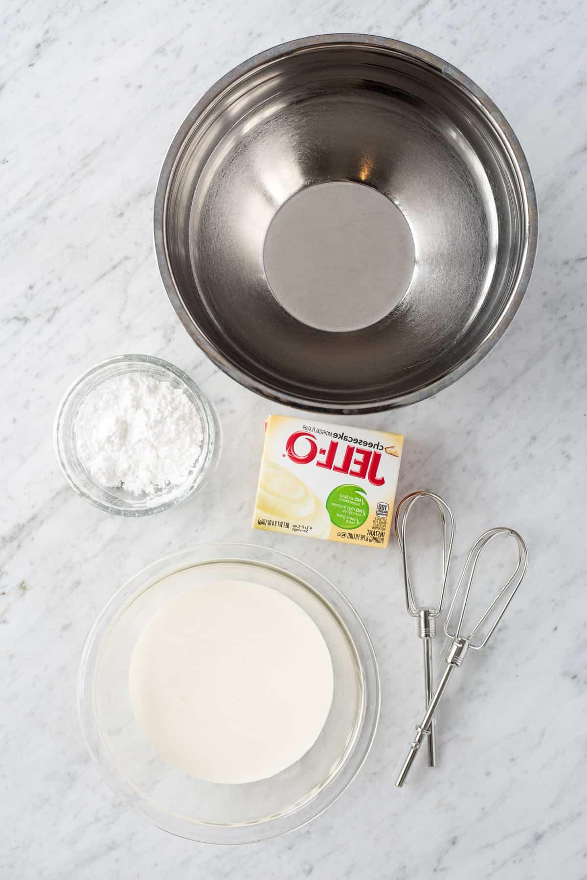 Come fare la panna montata al cheesecake stabilizzata che puoi usare su torte, cupcake, crostate e come salsa per frutta! Immagina questa panna montata al cheesecake su una crostata di fragole! #pannamonata #pannamonataaromatizzata #pannamonatacheesecake Ingredienti per fare la panna montata al cheesecake - ciotola di metallo, zucchero a velo, panna fresca, preparato istantaneo per budino al cheesecake e fruste