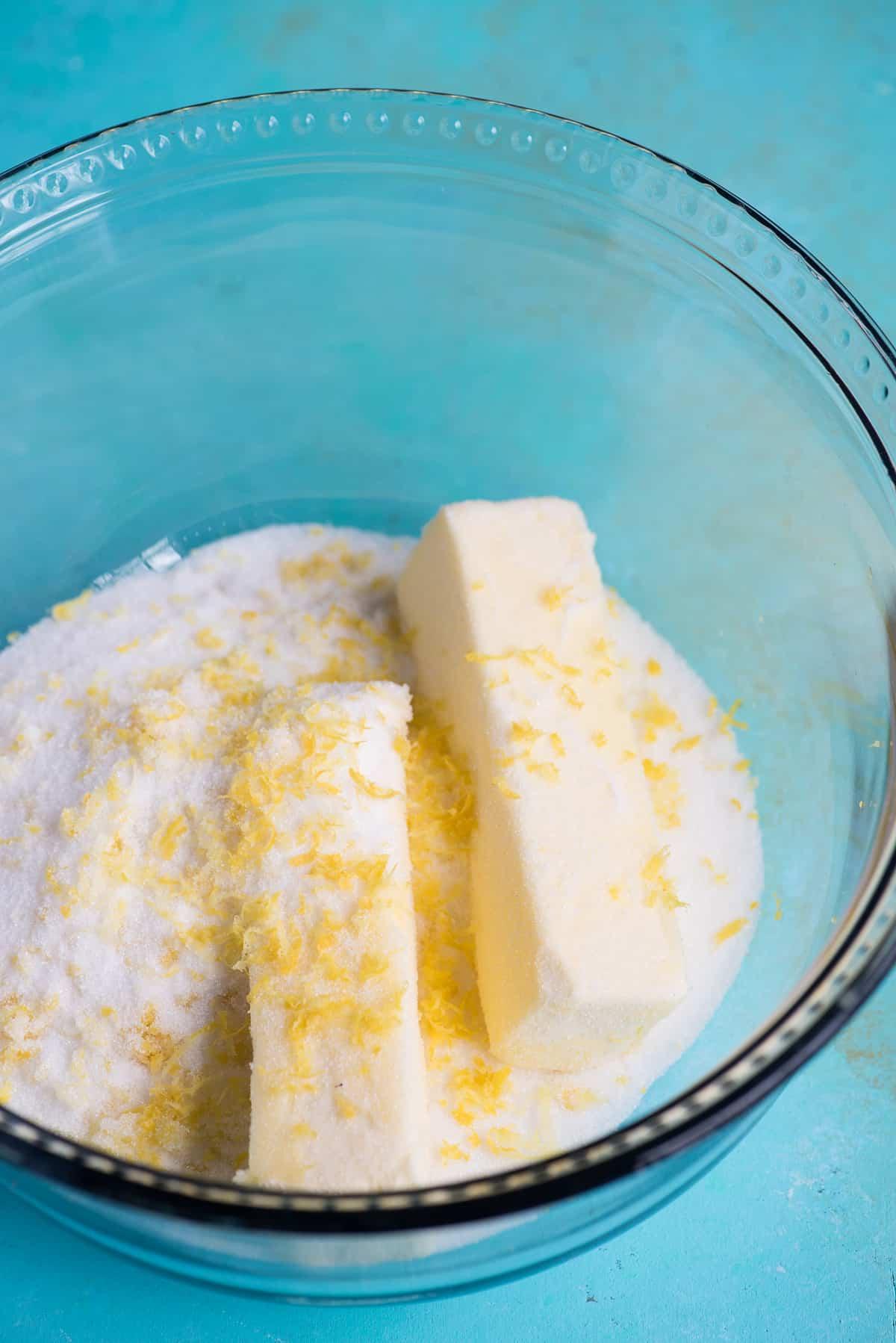 Ricetta Biscotti al Limone 4 Burro, zucchero semolato e scorza di limone in una ciotola di vetro su sfondo blu