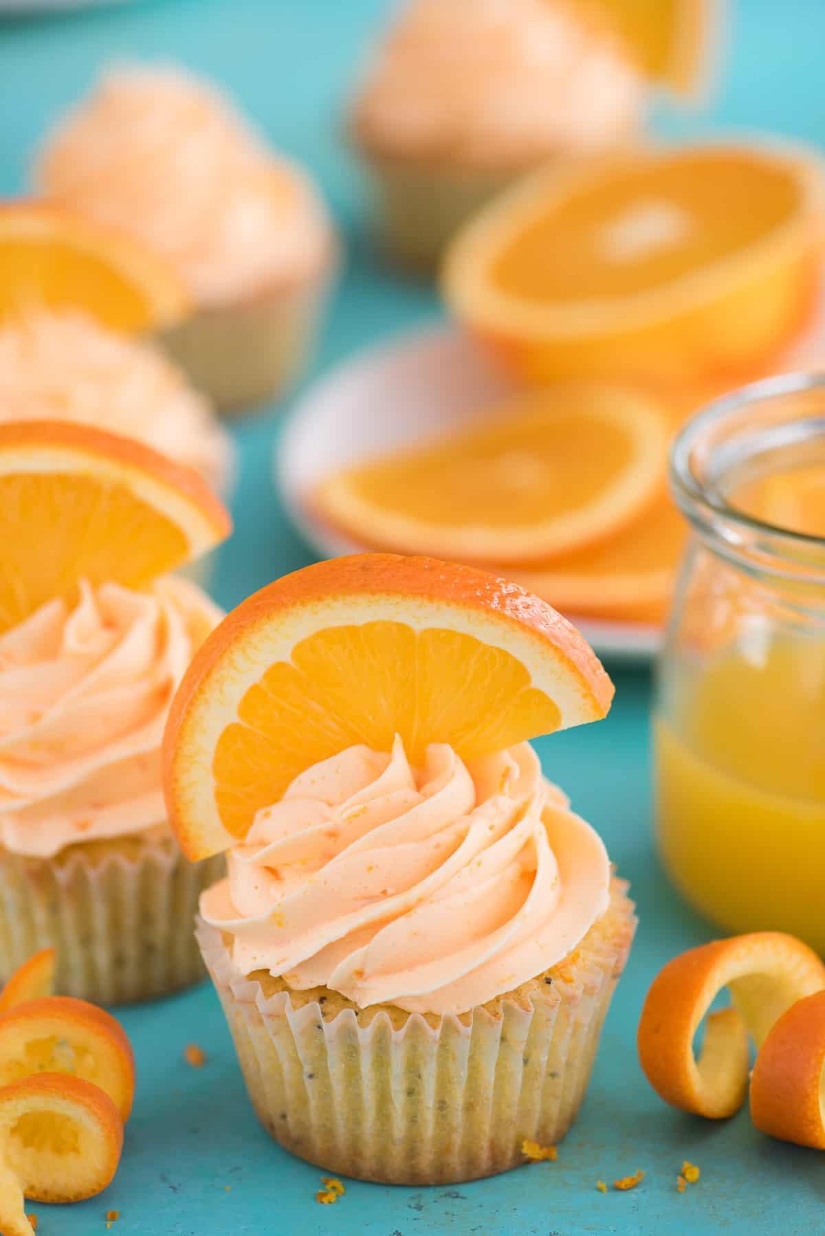 I Cupcake all'Arancia e Semi di Papavero sono una ricetta unica di cupcake agrumati, realizzati con vero succo e scorza d'arancia! Cupcake all'Arancia e Semi di Papavero con fetta d'arancia su sfondo blu