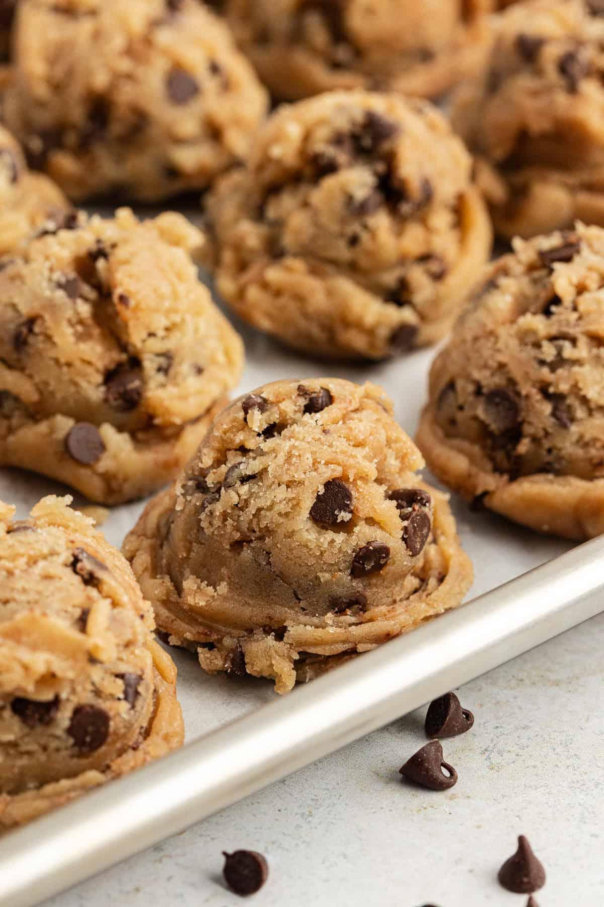 **Semplice Impasto per Biscotti Commestibile** 4 chocolate chip cookie dough balls in rows on a baking sheet