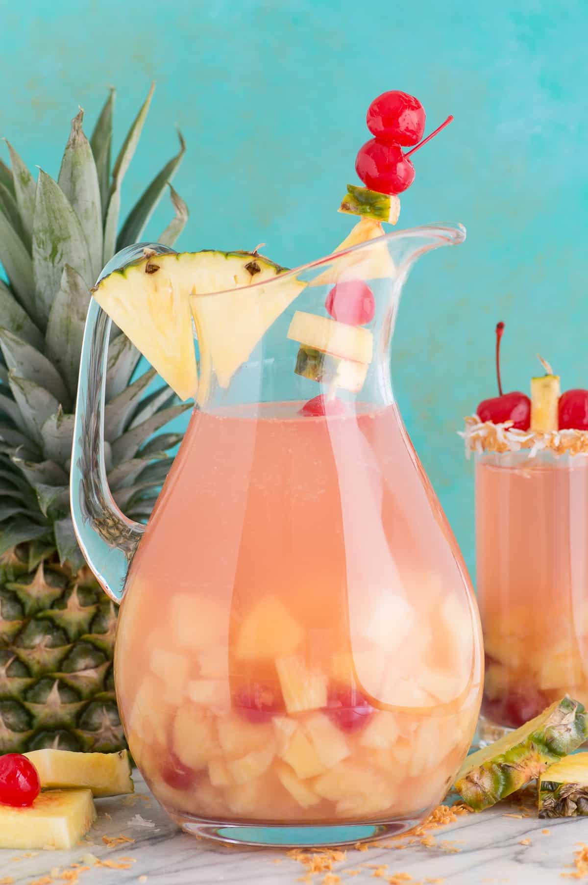 Sangria Piña Colada super facile e tropicale con 5 ingredienti è una bevanda estiva rinfrescante! Questo punch alcolico di sangria ne fa abbastanza per servire una folla. #pinacoladasangria #sangria Sangria Piña Colada in una caraffa di vetro con ananas e ciliegia