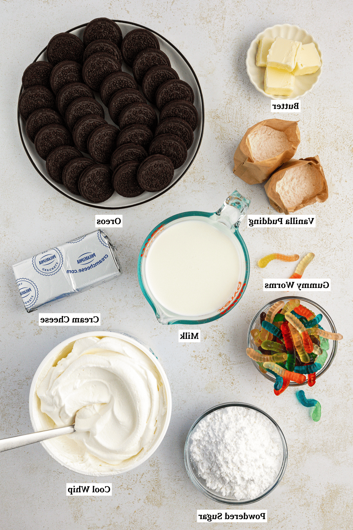 La migliore ricetta per la Torta al Fango 4 Vista dall'alto degli ingredienti per la torta di terra, inclusi burro, preparato per budino istantaneo alla vaniglia, latte, Oreo, vermi gommosi, crema di formaggio, Cool Whip e zucchero a velo