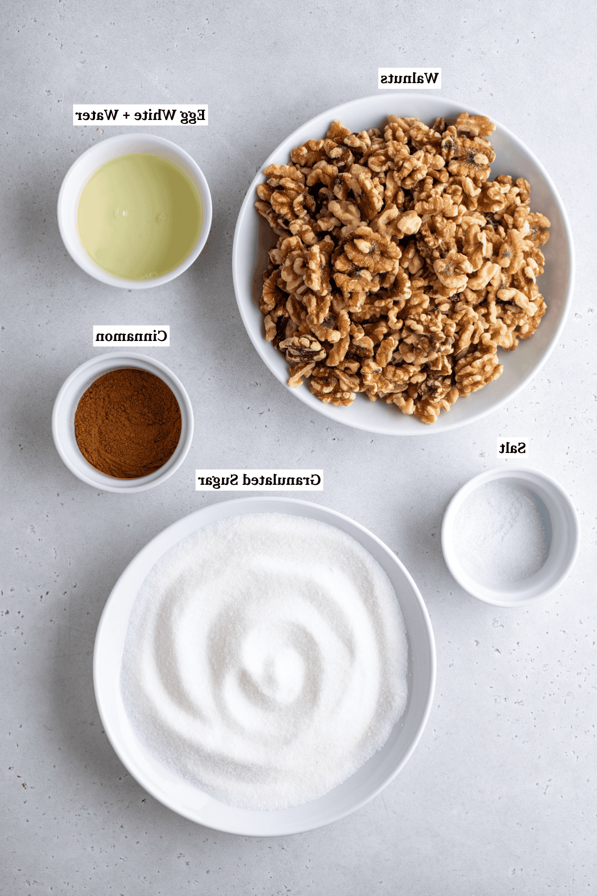 vista dall'alto degli ingredienti per le noci pralinate, tra cui noci, albumi, acqua, sale, cannella e zucchero semolato