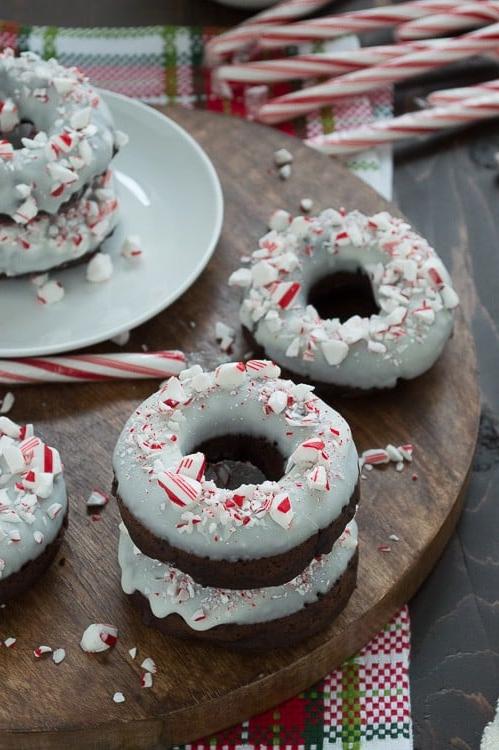 Ciambelle al cioccolato cotte al forno, aromatizzate alla menta piperita, guarnite con cioccolato bianco e bastoncini di zucchero tritati.