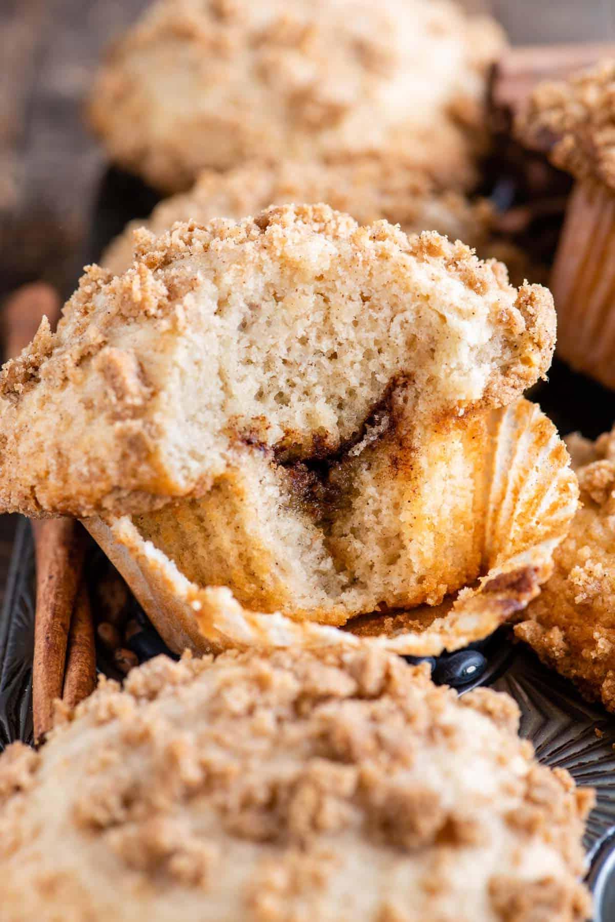 Muffin alla Sbriciolata 4 muffin al caffè con un morso che mostra lo strato di cannella all'interno nella teglia da muffin metallica