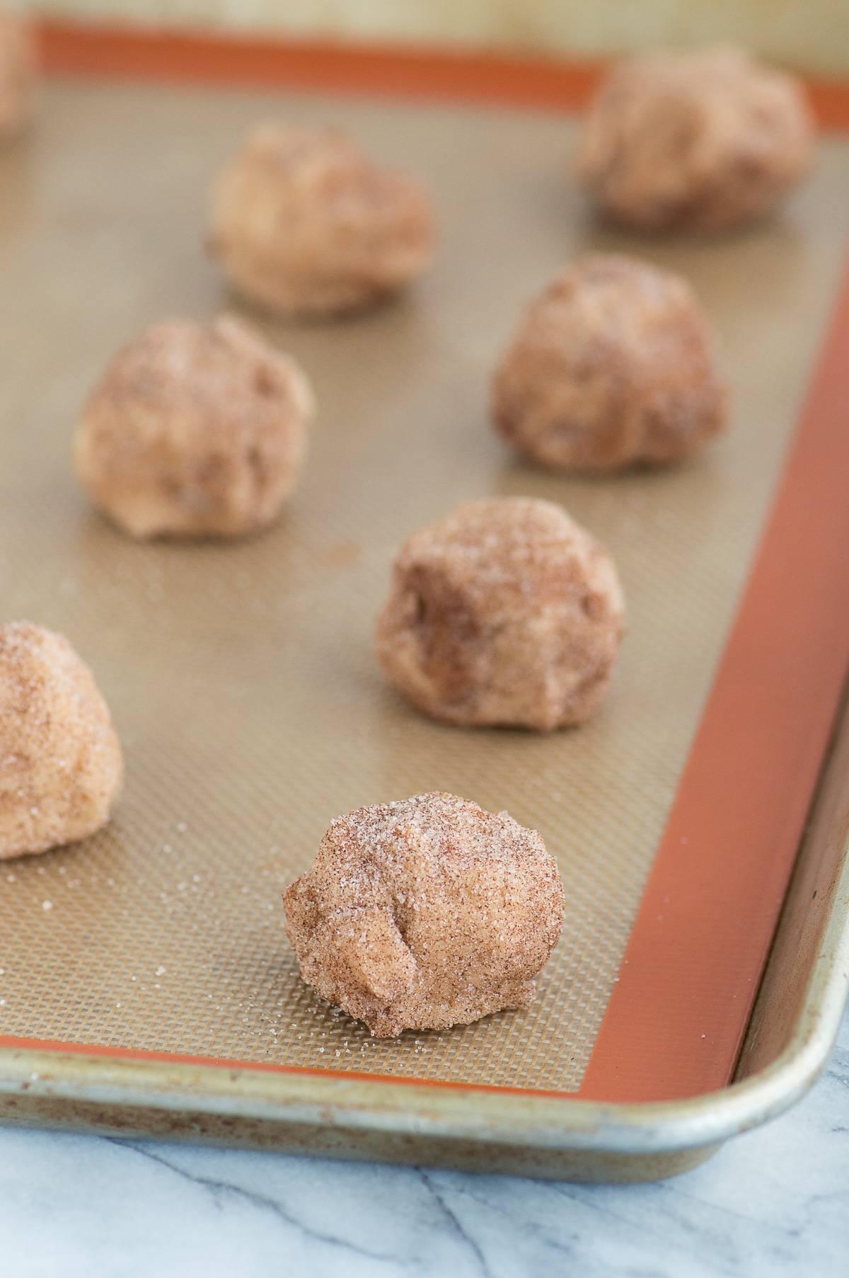 Snickerdoodles al Caramello e Mela 4 Palline di impasto per snickerdoodle alle mele caramellate allineate su un tappetino di silicone su una teglia metallica