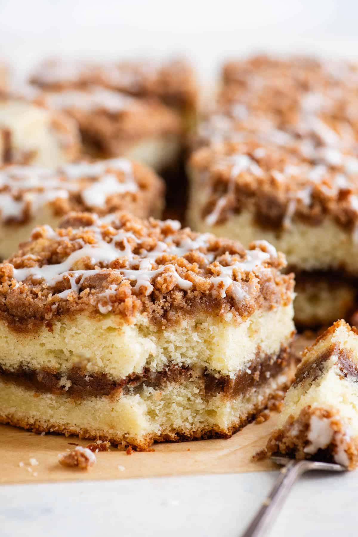 Ricetta Torta Umida al Caffè 4 Una fetta di torta al caffè con un morso preso, poggiata su una forchetta accanto alla fetta e altre fette di torta sullo sfondo