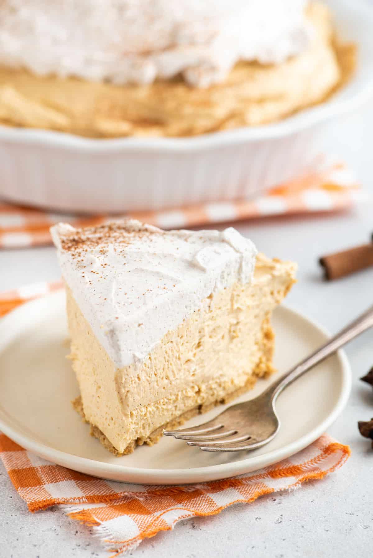 Questa torta di zucca senza cottura, veloce e facile, è leggera e cremosa - una deliziosa variante della classica torta di zucca. Una forchetta è appoggiata accanto a una fetta di torta di zucca senza cottura.