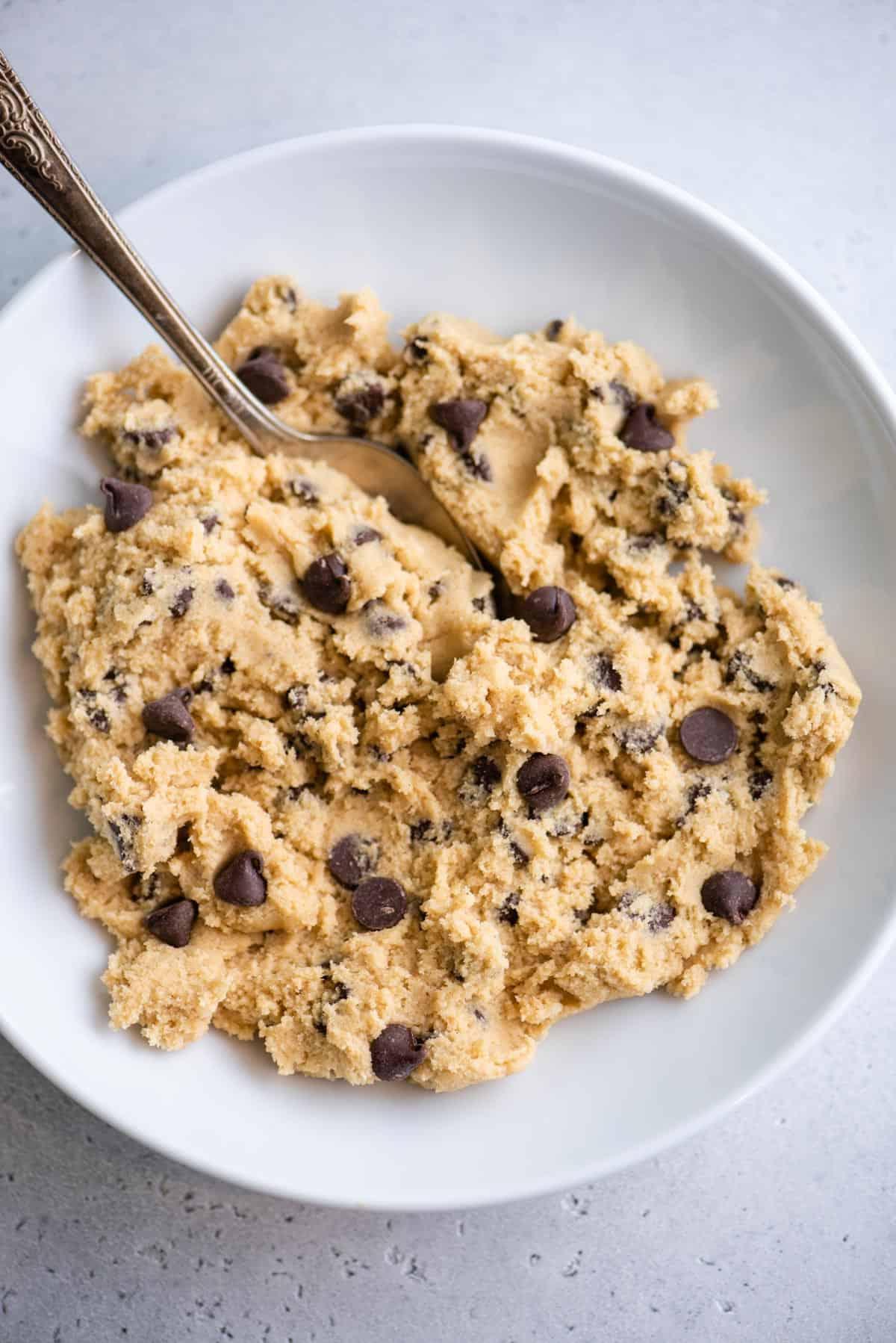 Se ami i biscotti morbidi e gommosi, adorerai questi biscotti con gocce di cioccolato in piccola quantità. Ne produce 6, perfetti per soddisfare una voglia! Visuale dall'alto dell'impasto dei biscotti con gocce di cioccolato in una ciotola con un cucchiaio