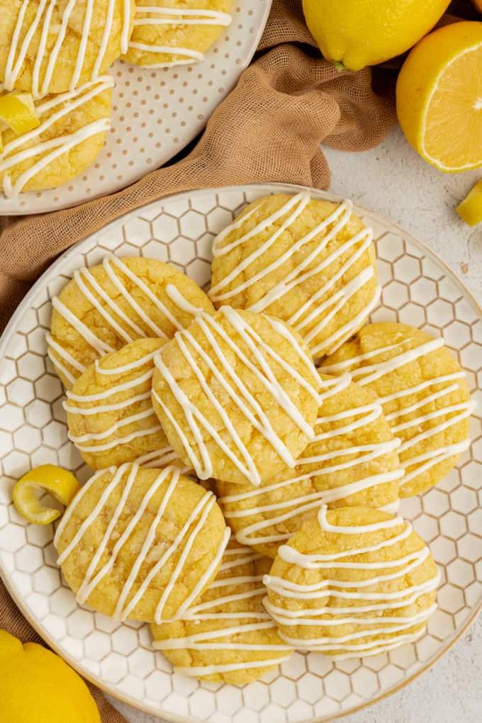 Fare Biscotti dal Mix per Torte 35 Biscotti al limone con preparato per torte su un piatto a nido d'ape circondato da panno beige, limoni e un altro piatto di biscotti sullo sfondo