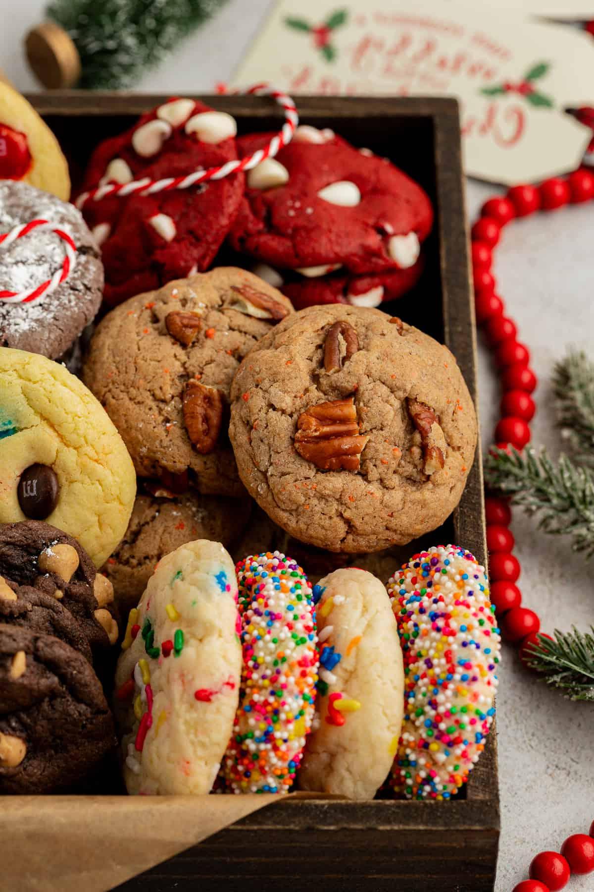 Fare Biscotti dal Mix per Torte 39 Assortimento di biscotti con preparato per torte di diversi gusti in una scatola di legno con carta marrone circondata da perline rosse, rami di pino e spago rosso e bianco