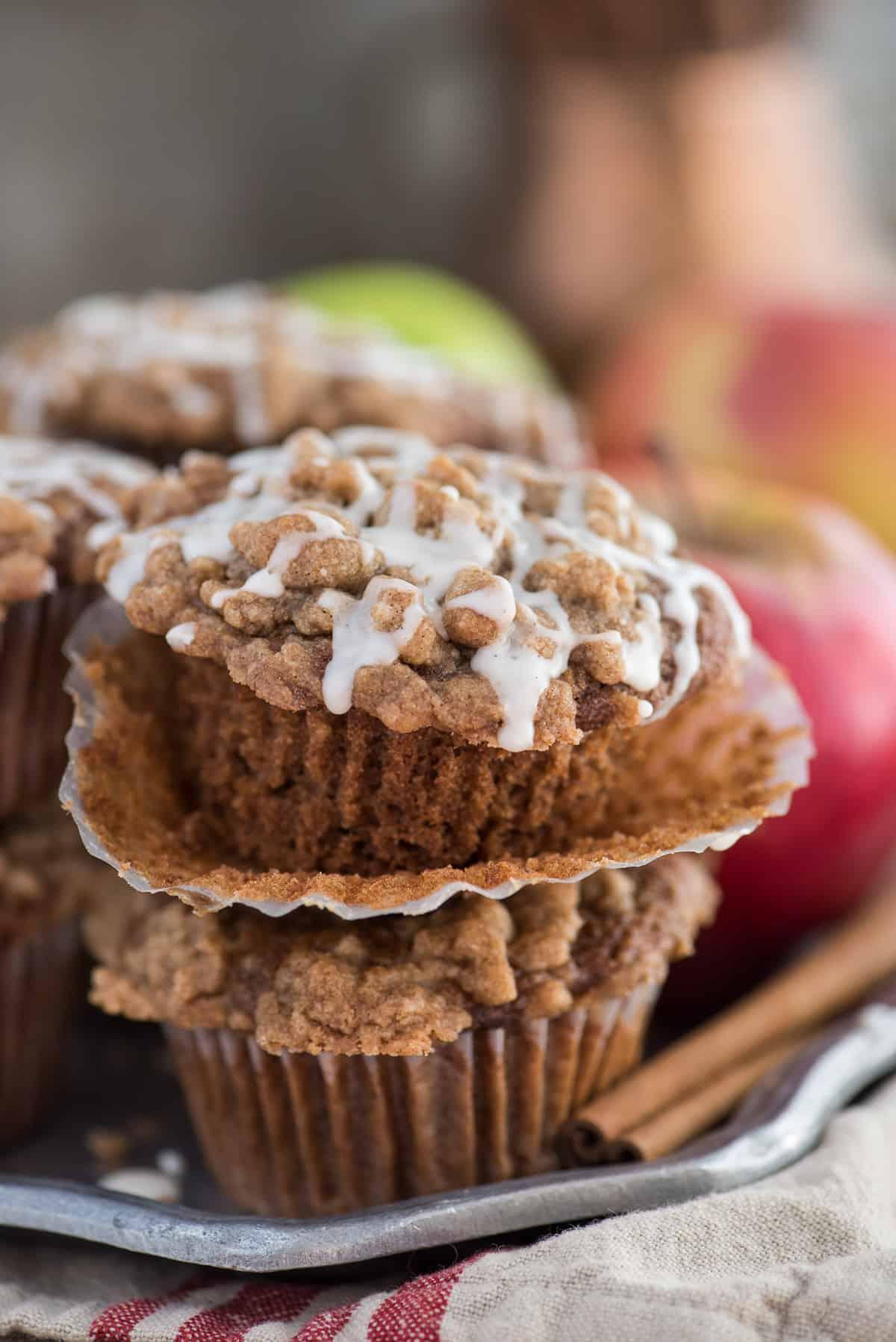 Muffin speziati alla salsa di mele con crumble e glassa bianca su un piatto di metallo, con mele sullo sfondo