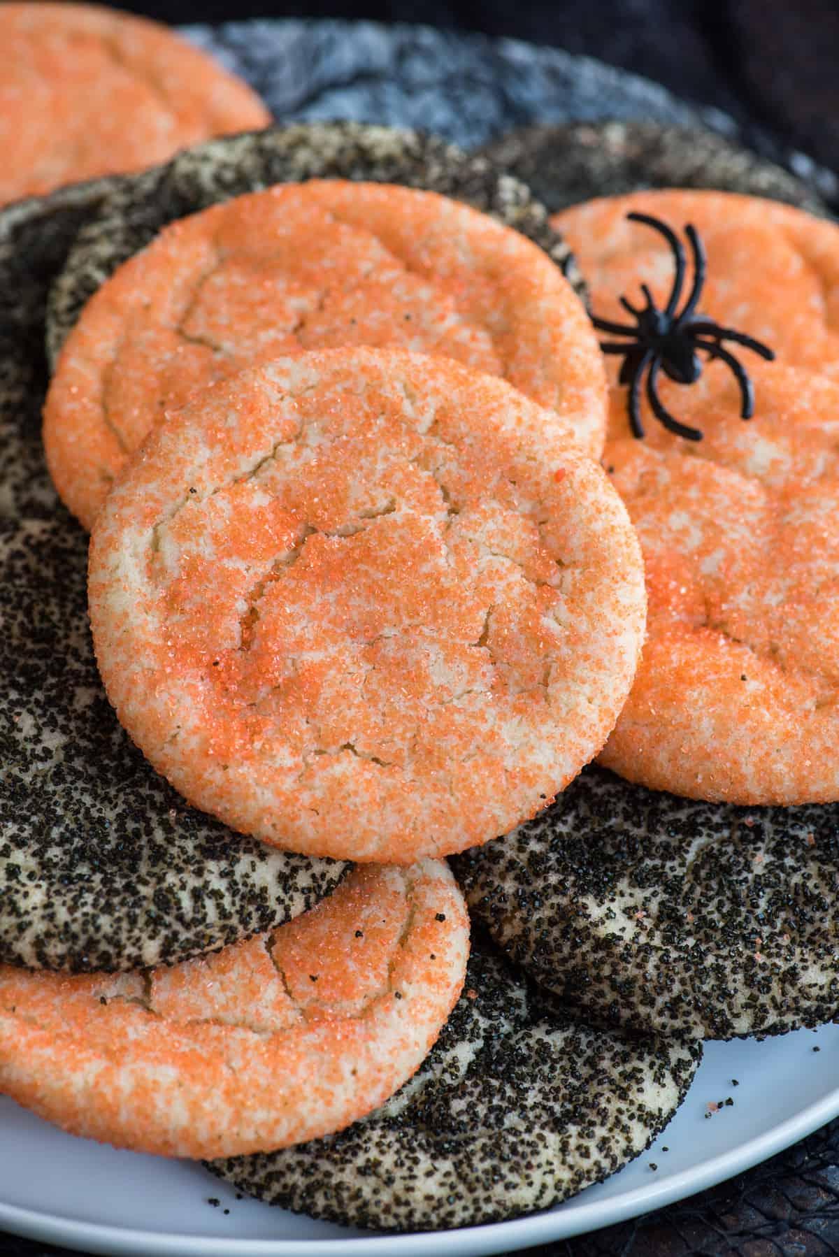 Semplici Biscotti di Zucchero di Halloween 5 Biscotti di zucchero arancioni e neri ammucchiati su piatto bianco con tessuto nero su sfondo nero