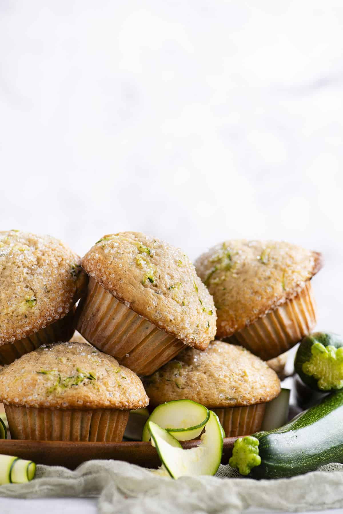 Migliori Muffin alle Zucchine 5 Un mucchio di muffin di zucchine su un piatto di legno con zucchine intere e fette di zucchine sparse intorno