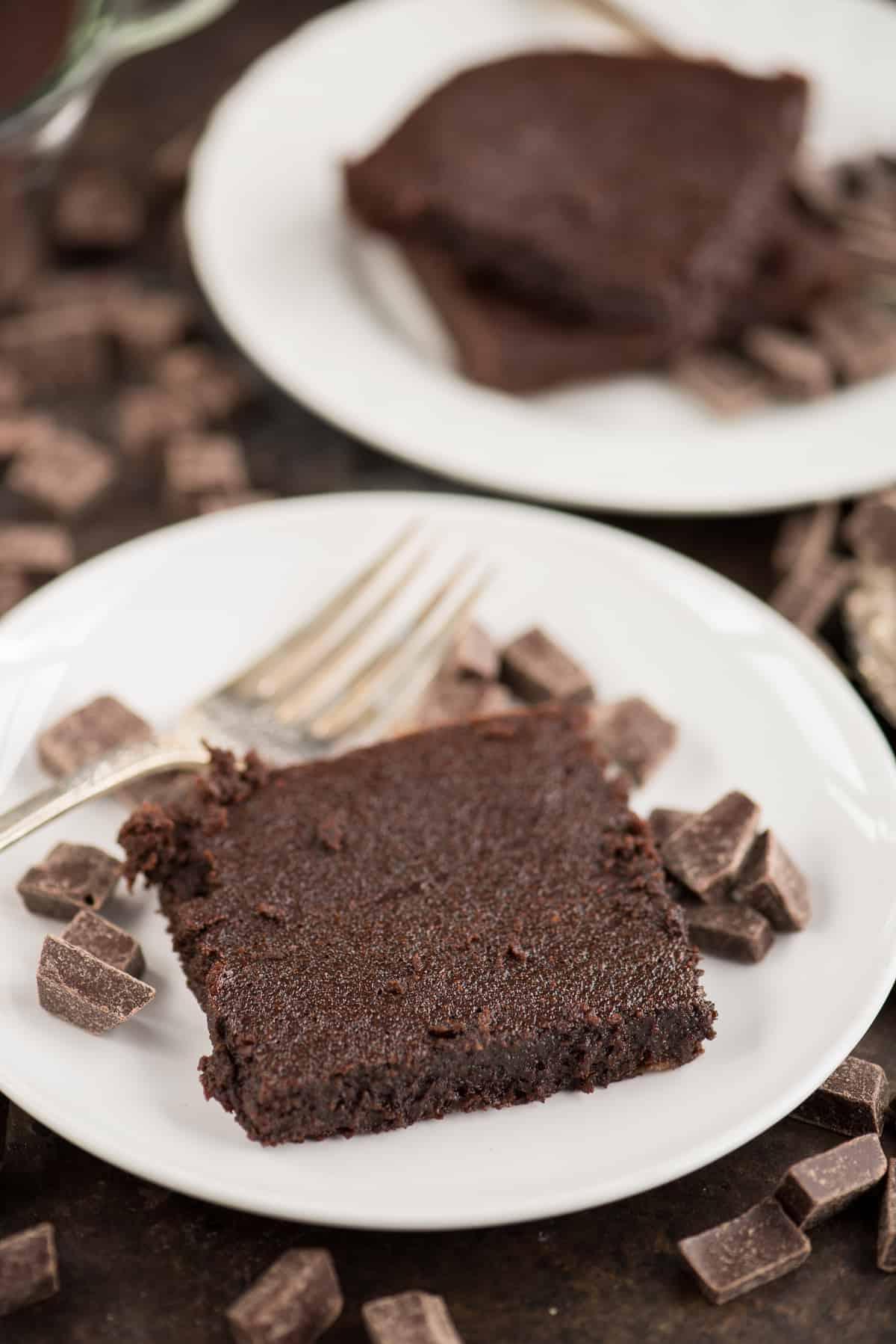 I brownies fondenti e salutari dei vostri sogni! Senza zucchero raffinato, burro o olio, con ingredienti comuni e un incredibile gusto fondente. Solo 174 calorie a fetta! Un brownie fondente salutare con piccoli pezzi di cioccolato e una forchetta d'argento su un piatto bianco.