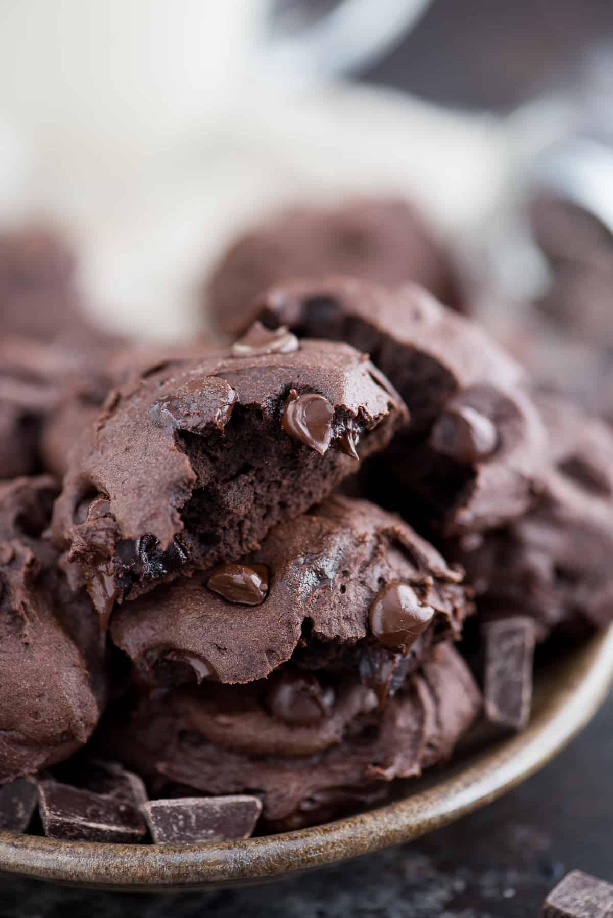 Biscotti Sani al Cioccolato Fondente e Olio di Cocco - Stimati a 150 calorie. Adoro che la ricetta richieda ingredienti comuni e senza zucchero raffinato, burro o olio! Un biscotto sano al cioccolato fondente e olio di cocco morso, sopra altri biscotti in un piatto.