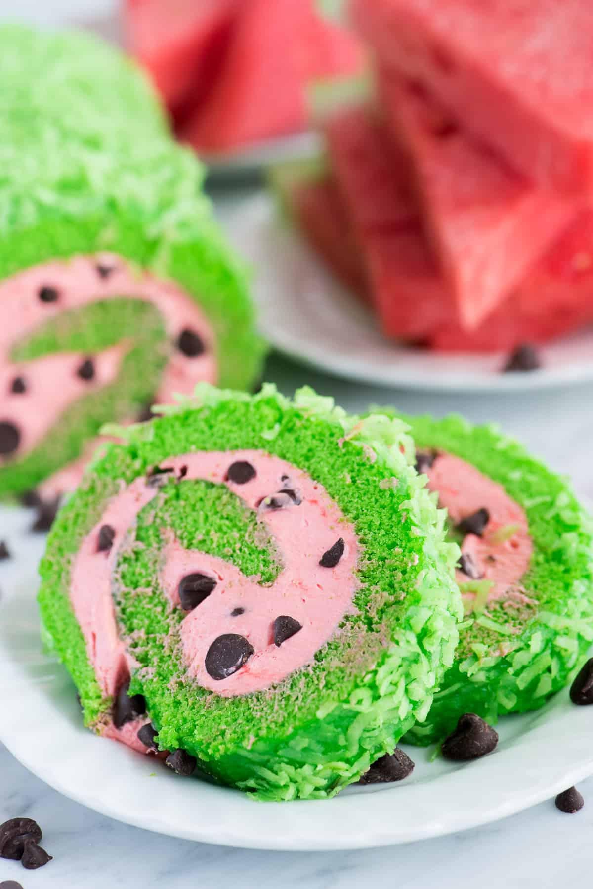 Una torta rotolo con ripieno rosa e gocce di cioccolato, distesa su un canovaccio spolverato di zucchero a velo, pronta per essere arrotolata.