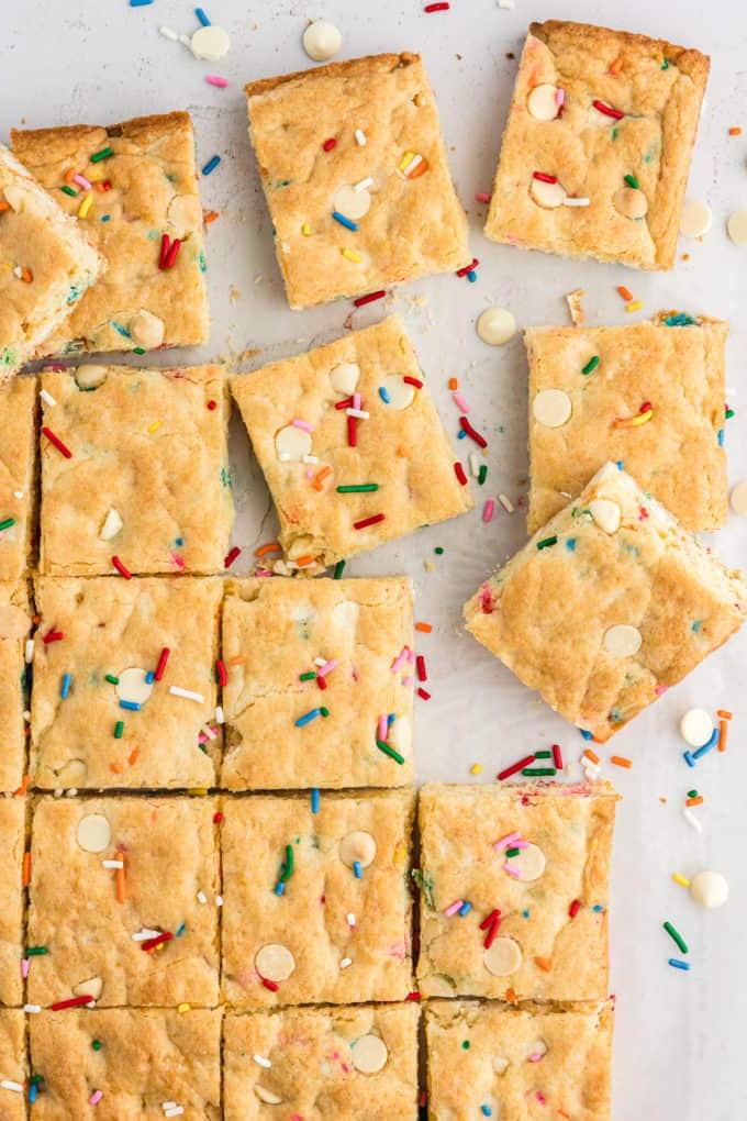 Barrette di biscotti da preparato per torte 5 rows of cut funfetti cake bars with some pulled out of the rows and arranged randomly, surrounded by white chocolate chips and sprinkles