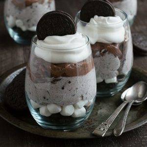 **Parfait Decadenti di Cheesecake al Cioccolato con Oreo** 6 Due bicchieri di parfait al cioccolato, cheesecake e Oreo, con cucchiaini su un vassoio metallico