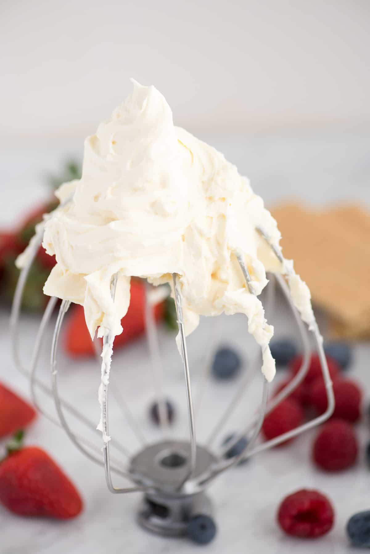 Come fare la panna montata al cheesecake stabilizzata che puoi usare su torte, cupcake, crostate e come salsa per frutta! Immagina questa panna montata al cheesecake su una crostata di fragole! #pannamonata #pannamonataaromatizzata #pannamonatacheesecake Frusta KitchenAid con panna montata al cheesecake e frutti di bosco sullo sfondo