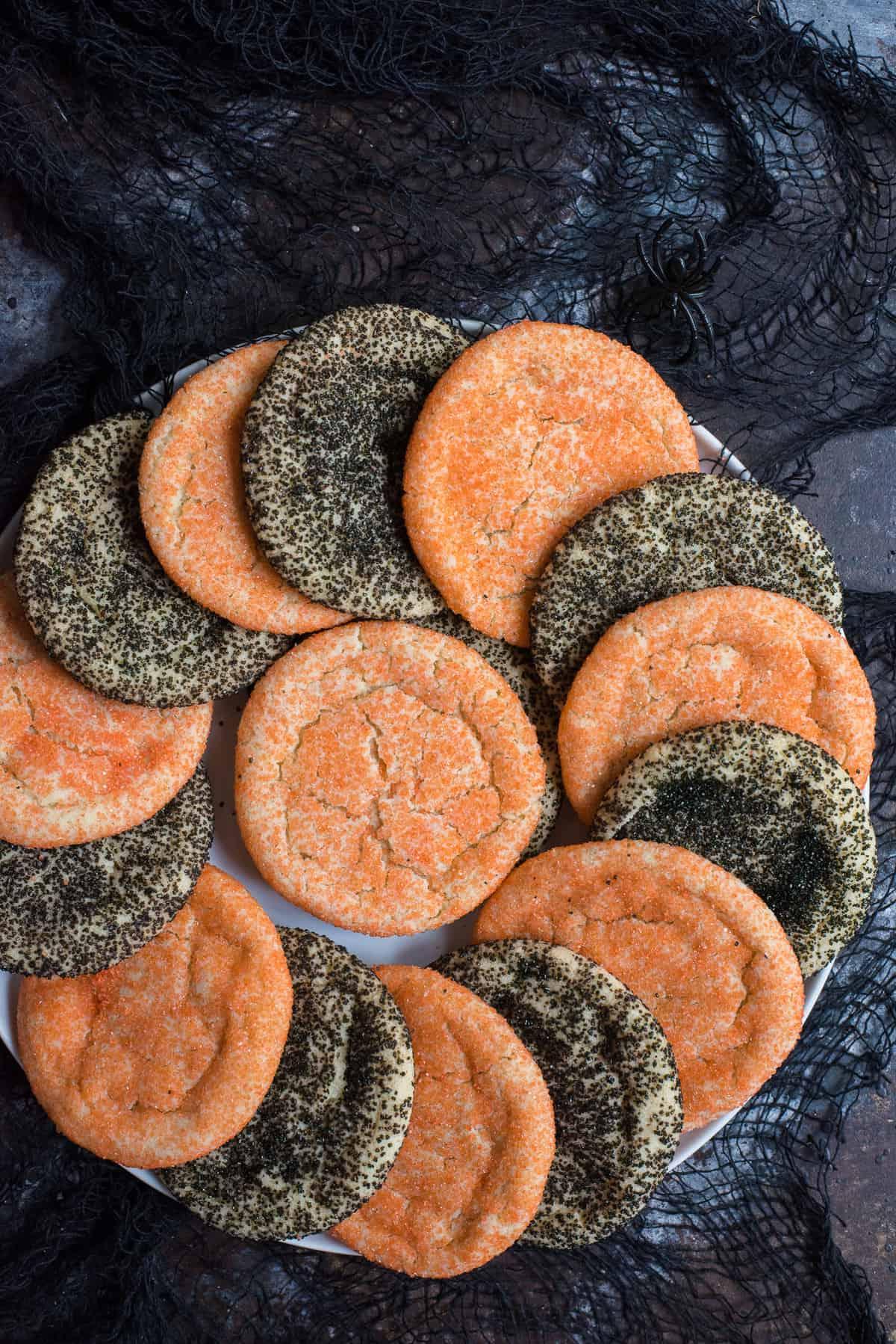 Semplici Biscotti di Zucchero di Halloween 6 Biscotti di zucchero arancioni e neri a spirale su piatto bianco con tessuto nero su sfondo nero