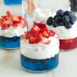 Coppette di Frutta e Gelatina per il 4 Luglio 6 Tre bicchierini di vetro con bicchierini di gelatina festivi del 4 luglio: gelatina blu a strati con mirtilli e panna montata, uno sormontato da mirtilli extra, mentre gli altri hanno fragole su panna montata su gelatina rossa o blu.