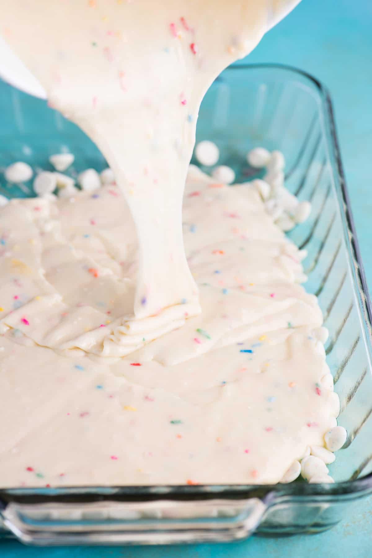 Questa torta terremoto funfetti è un mix per torta bianca arricchito con zuccherini e gocce di cioccolato funfetti. Lo strato di glassa al formaggio cremoso si fonde nella torta creando crepe e fessure in superficie. #earthquakecake #funfetticake #cake Impasto per torta funfetti versato in una teglia di vetro 9x13 pollici