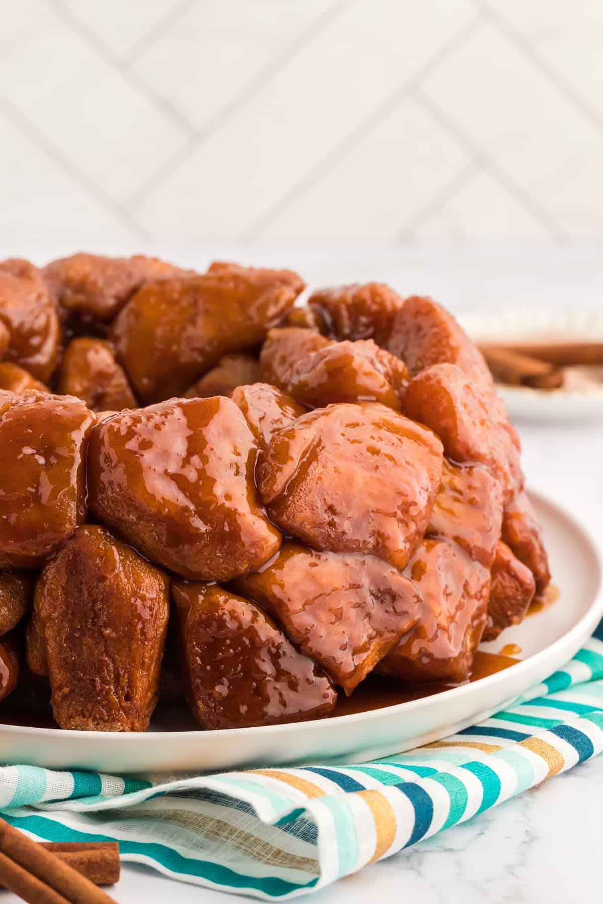 Pane delle scimmie di biscotti 6 Monkey Bread su un piatto bianco su un telo a strisce oro, blu e turchese con bastoncini di cannella accanto