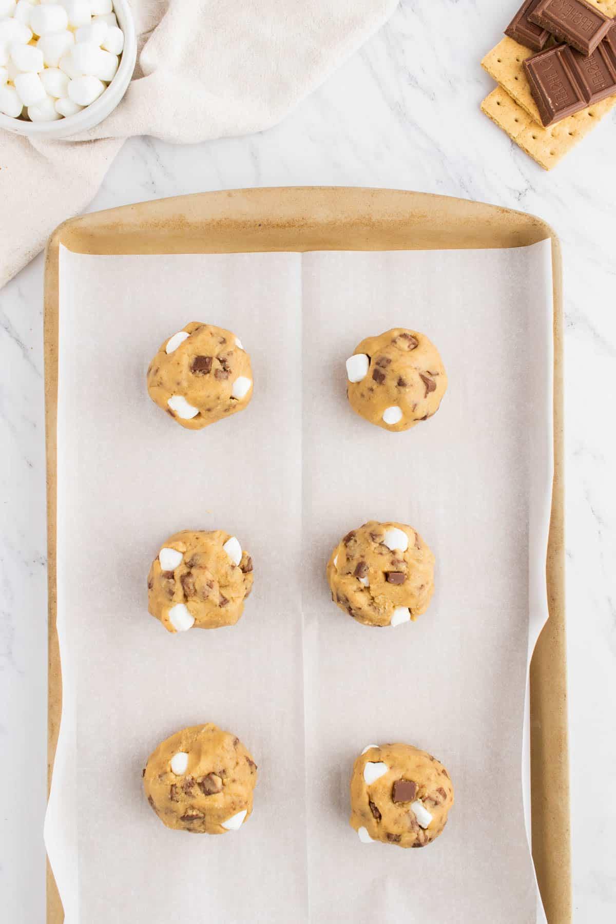 Ricetta Biscotti S'mores con Graham Crackers 6 palline di impasto per biscotti s'mores allineate su carta da forno su una teglia