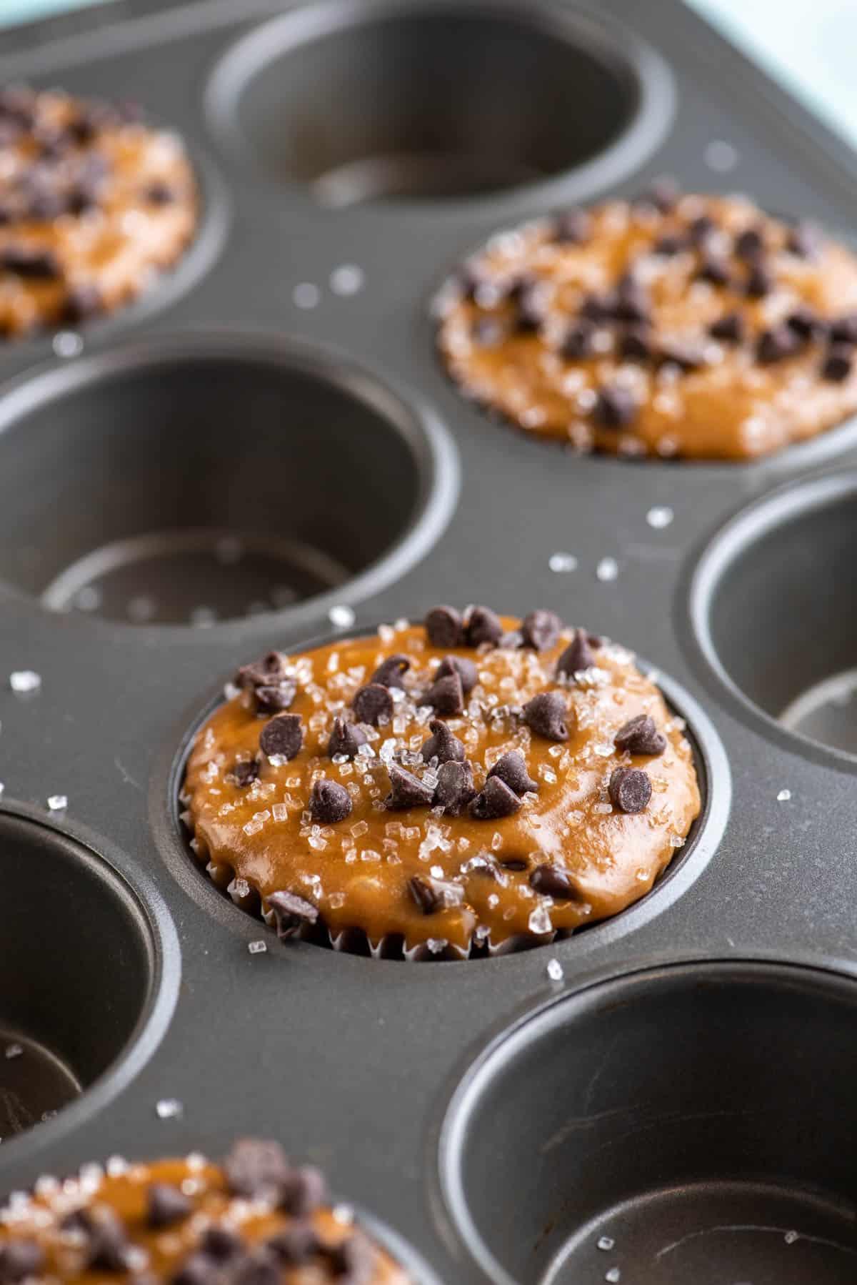 impasto di muffin al cappuccino con gocce di cioccolato che riempie un foro sì e uno no di una teglia per muffin, condito con mini gocce di cioccolato e spolverato di zucchero semolato grosso