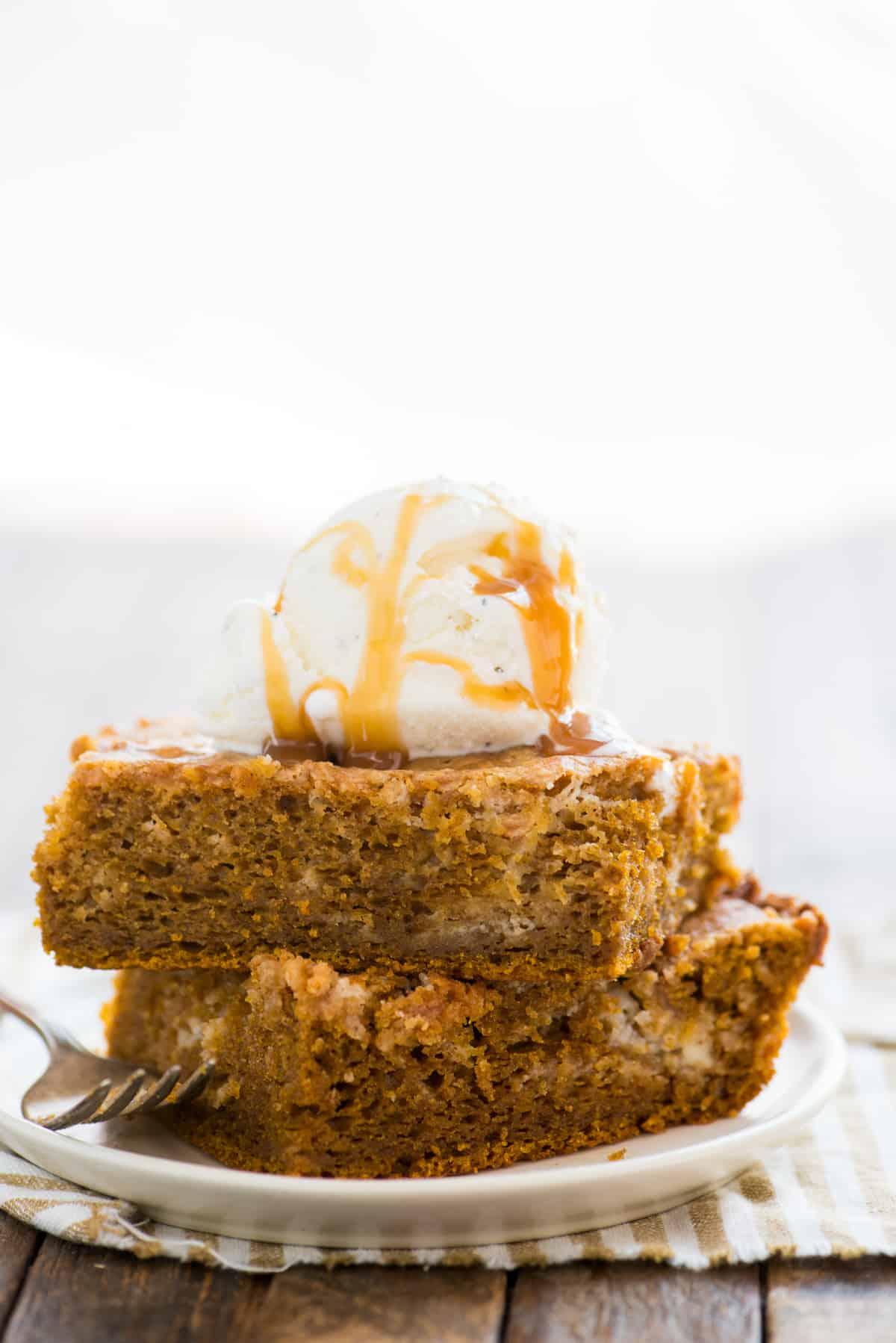 Due fette di torta terremoto alla zucca impilate l'una sull'altra su piatto bianco con una pallina di gelato alla vaniglia sopra