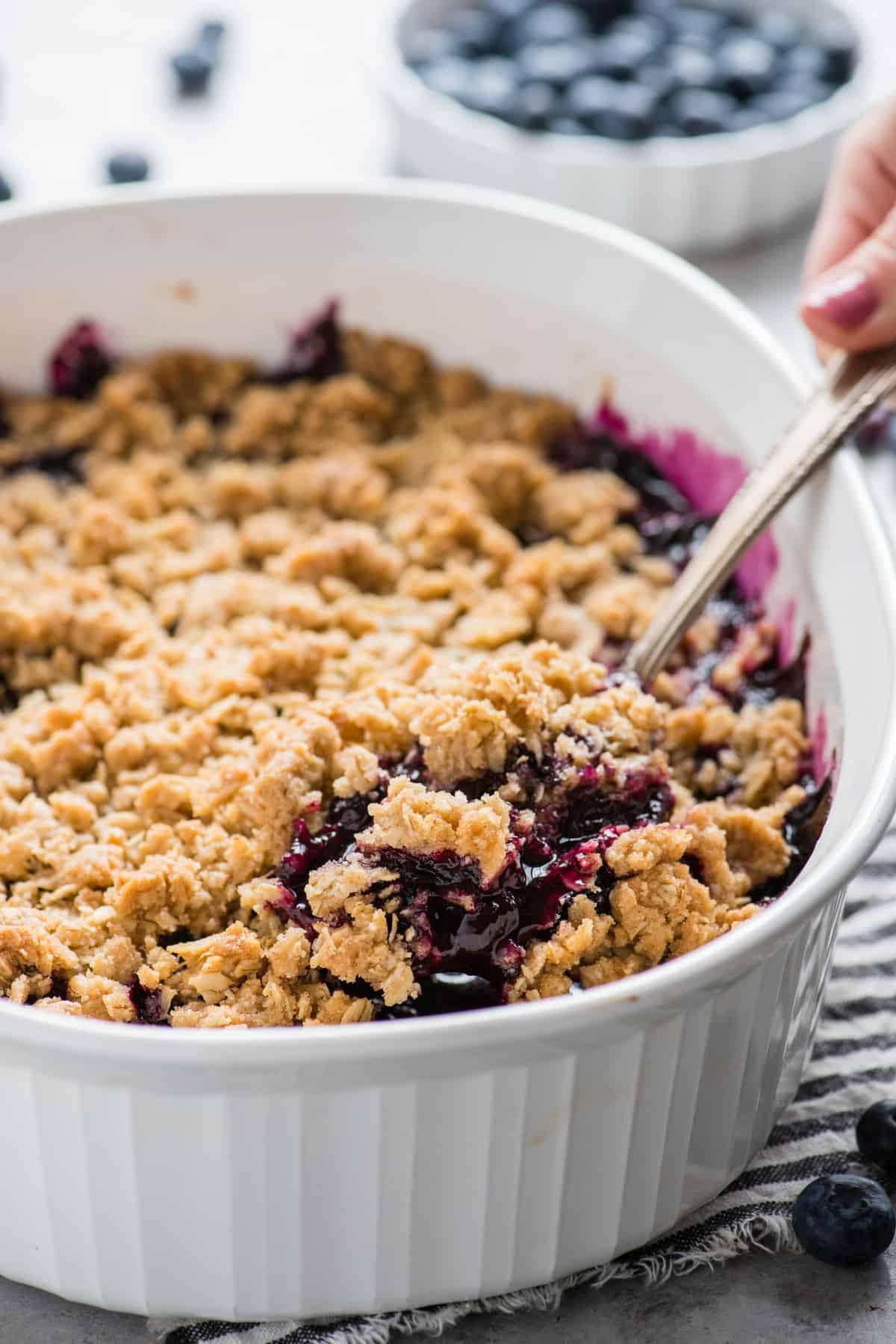 Crumble di Mirtilli Freschi 6 Crumble ai mirtilli in una teglia bianca con un cucchiaio di metallo