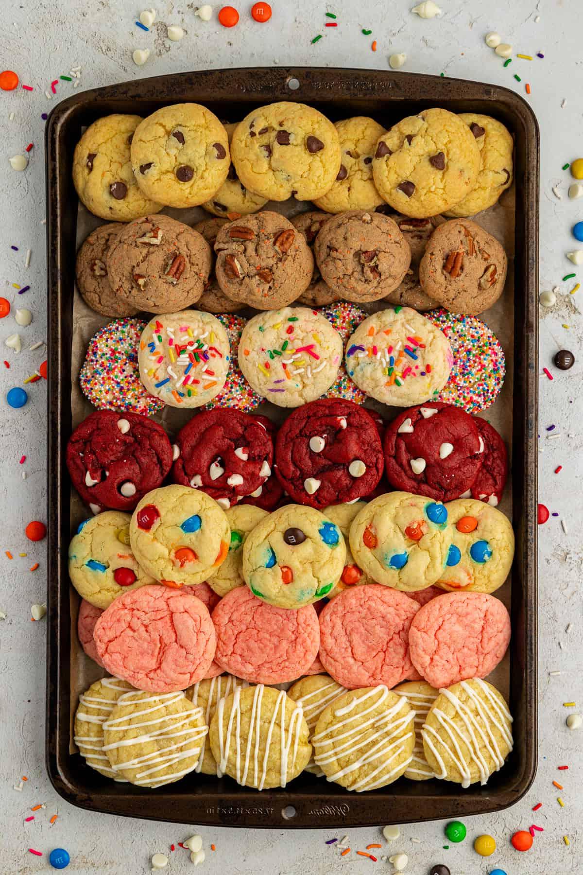 Fare Biscotti dal Mix per Torte 6 Fila di biscotti con preparato per torte di vari gusti impilati in diversi strati su una teglia circondata da M&M's, Reese's Pieces e codette colorate