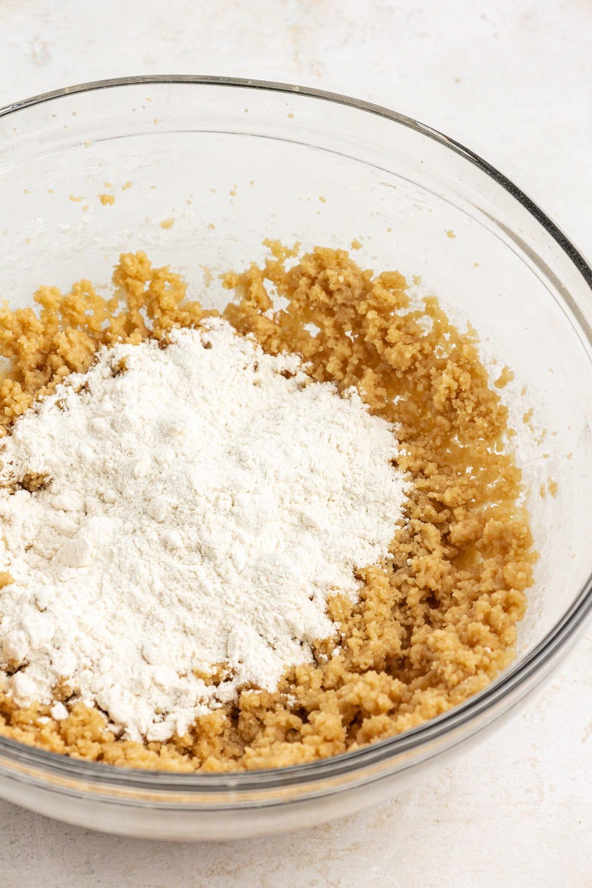 **Semplice Impasto per Biscotti Commestibile** 7 wet ingredients for edible cookie dough creamed together in a clear glass bowl with dry ingredients in a pile on top