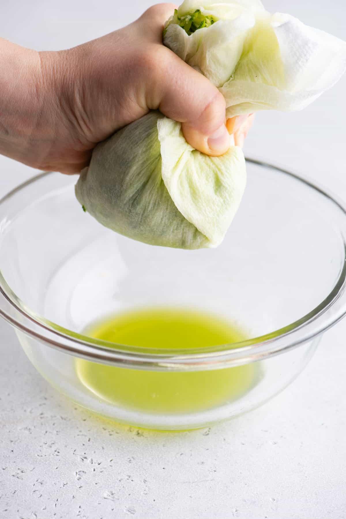 Migliori Muffin alle Zucchine 7 Un tovagliolo di carta pieno di zucchine grattugiate che viene strizzato sopra una ciotola di vetro trasparente per rilasciare l'umidità in eccesso