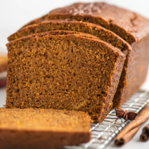 Una pagnotta di pane di zucca senza glutine è affettata e posizionata su un vassoio di raffreddamento a griglia.