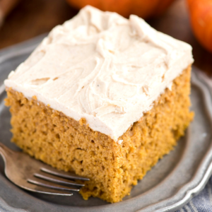 Facile Torta di Zucca da Mix 7 Una fetta quadrata di torta di zucca umida e facile con glassa bianca cremosa, posta su un piatto grigio, con una forchetta accanto.