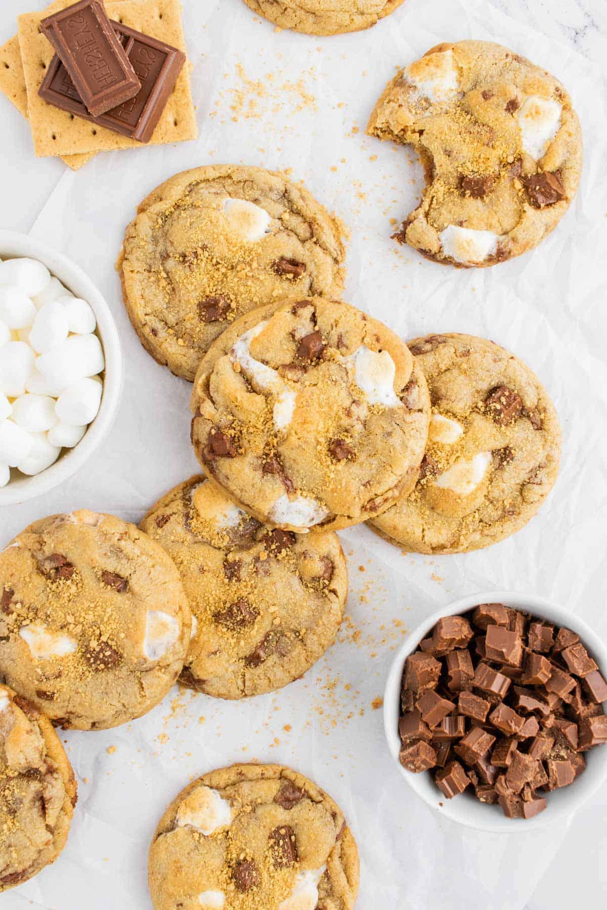 Ricetta Biscotti S'mores con Graham Crackers 7 una pila di biscotti s'mores con cracker Graham, cioccolato, marshmallow e un biscotto parzialmente mangiato disposti intorno