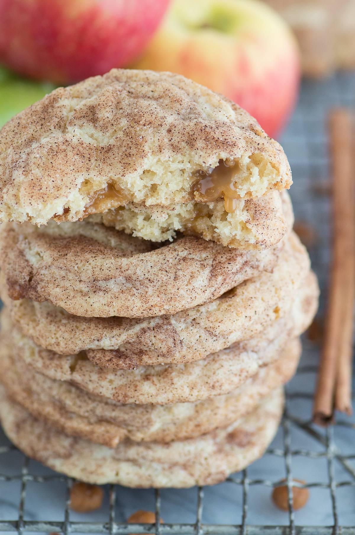 Snickerdoodles al Caramello e Mela 7 Biscotti snickerdoodle alle mele caramellate impilati su una griglia di raffreddamento metallica con mele sullo sfondo