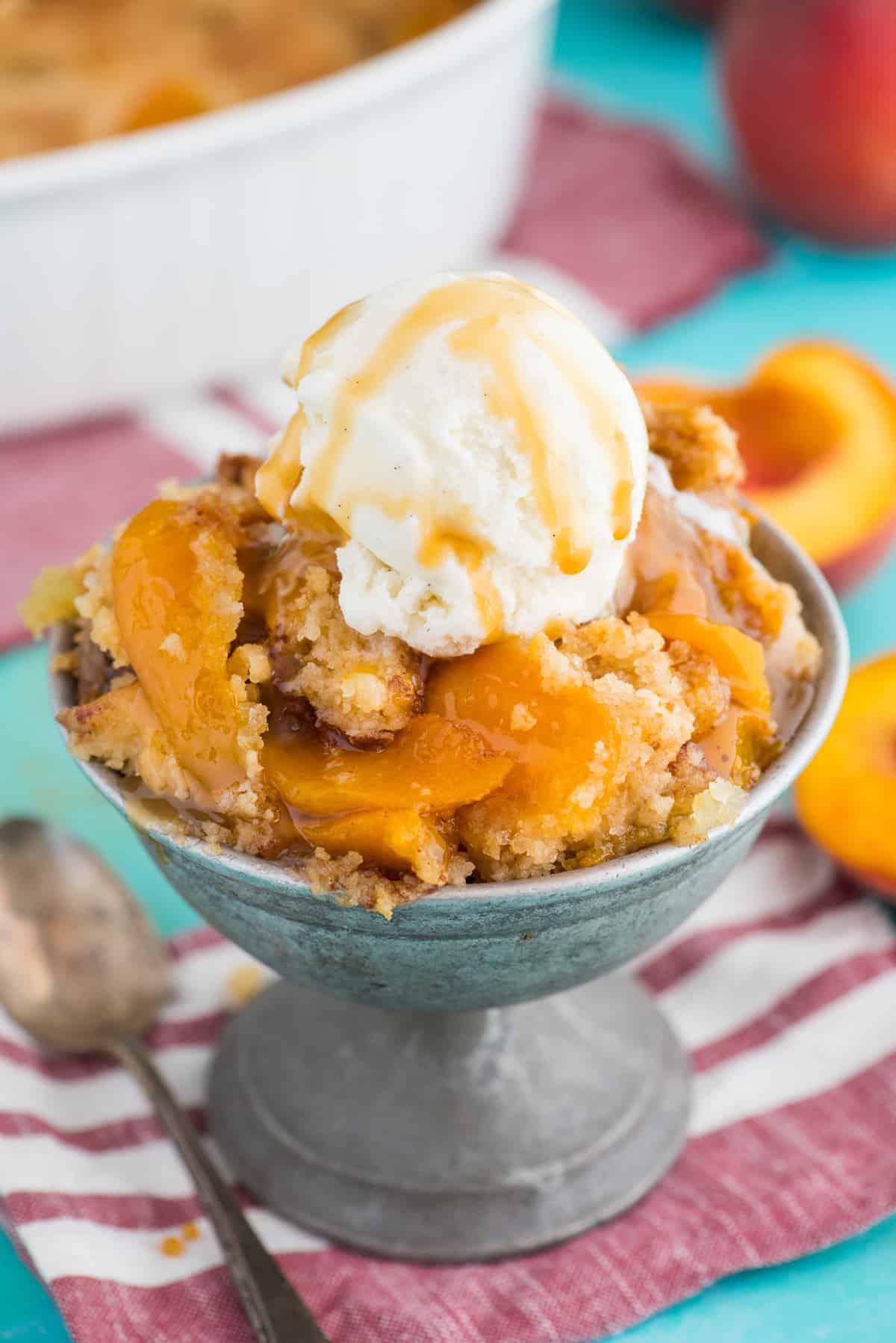 Torta Facile di Pesche con Preparato per Torta 7 torta di pesche dump cake in ciotola di metallo con cucchiaio di gelato alla vaniglia sopra