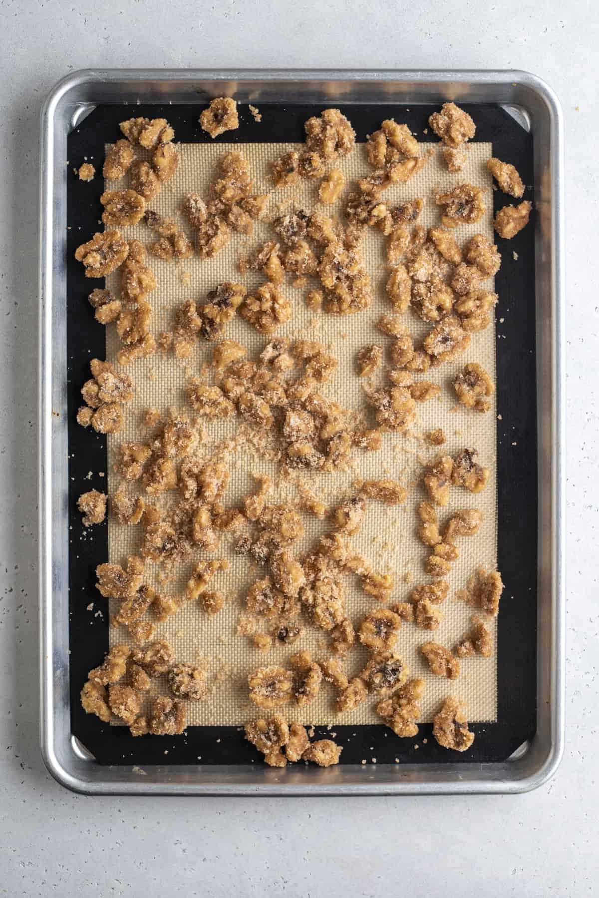 noci pralinate sparse su una teglia foderata con un tappetino da forno in silicone