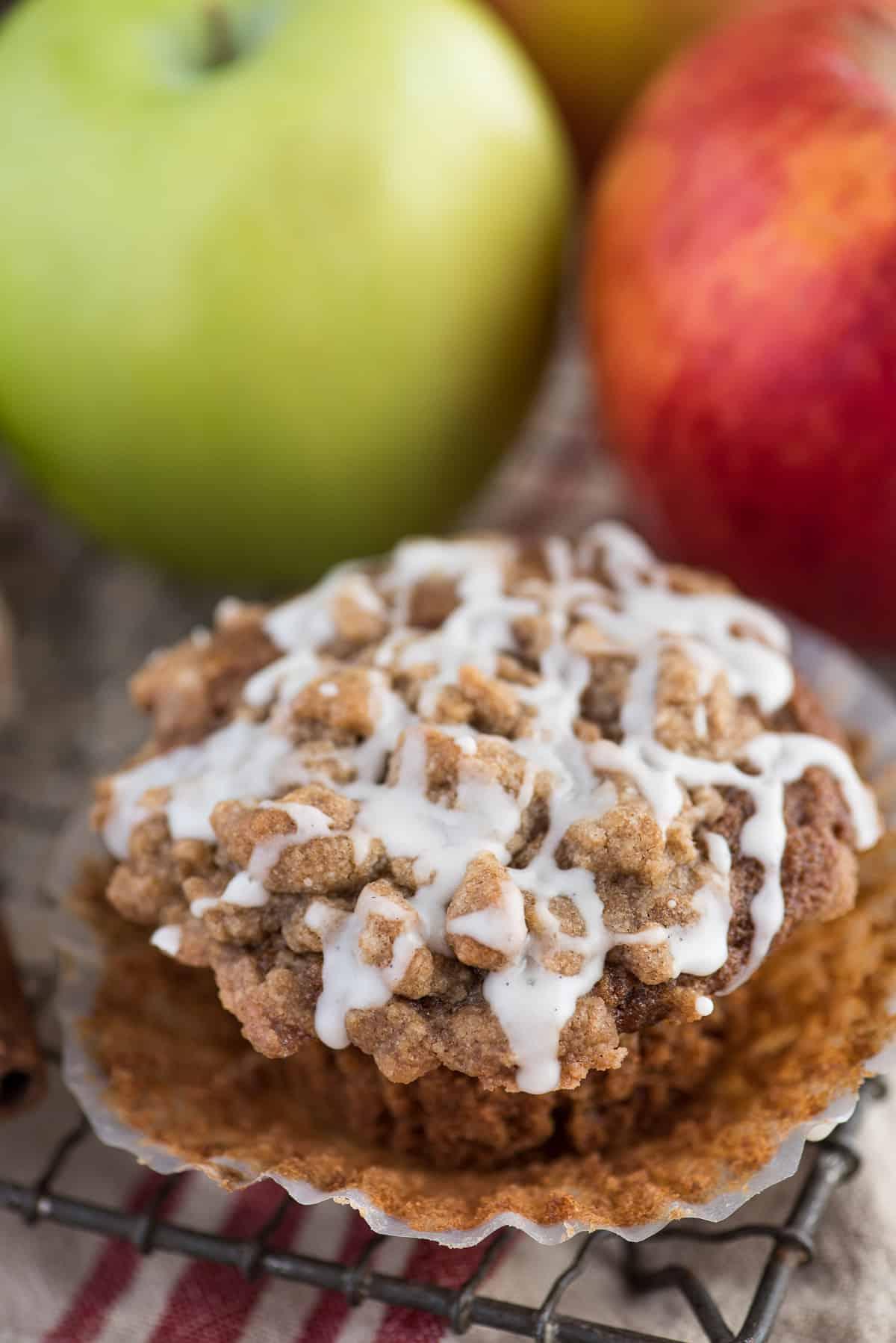Muffin speziati alla salsa di mele con crumble e glassa bianca su una griglia e mele sullo sfondo